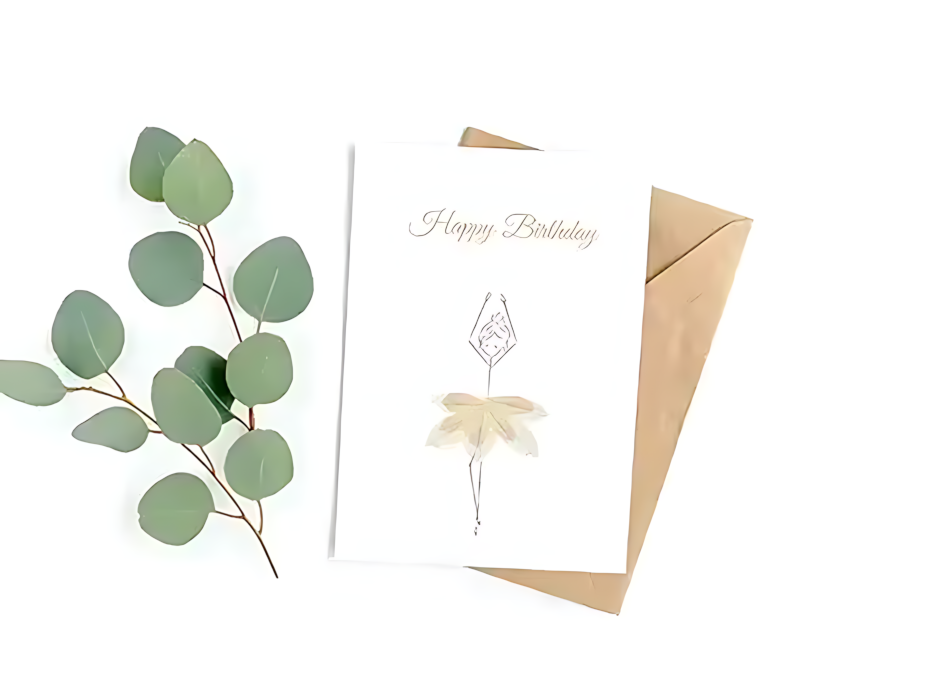 Eine weiße Geburtstagskarte mit goldener Schrift 'Happy Birthday' und einer filigranen Zeichnung einer Ballerina, deren Tutu aus hellen, getrockneten Blütenblättern gefertigt ist.